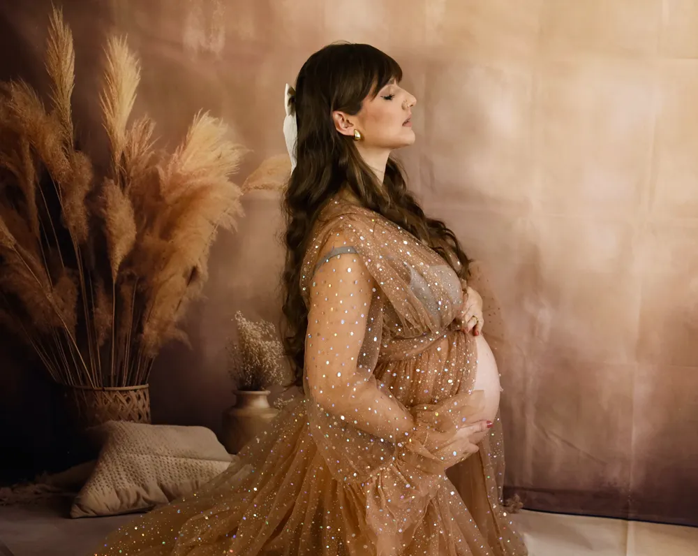 Schwangere im goldenen Glitzerkleid vor Pampasgras und warmem Hintergrund