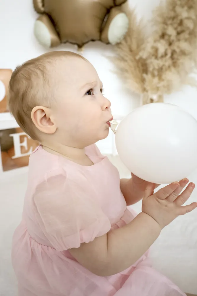 Kleinkind im rosa Kleid pustet in einen weißen Luftballon