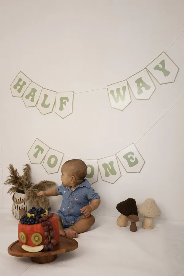 Baby beim Halbjahres-Shooting vor einer Girlande mit der Aufschrift Half way to one