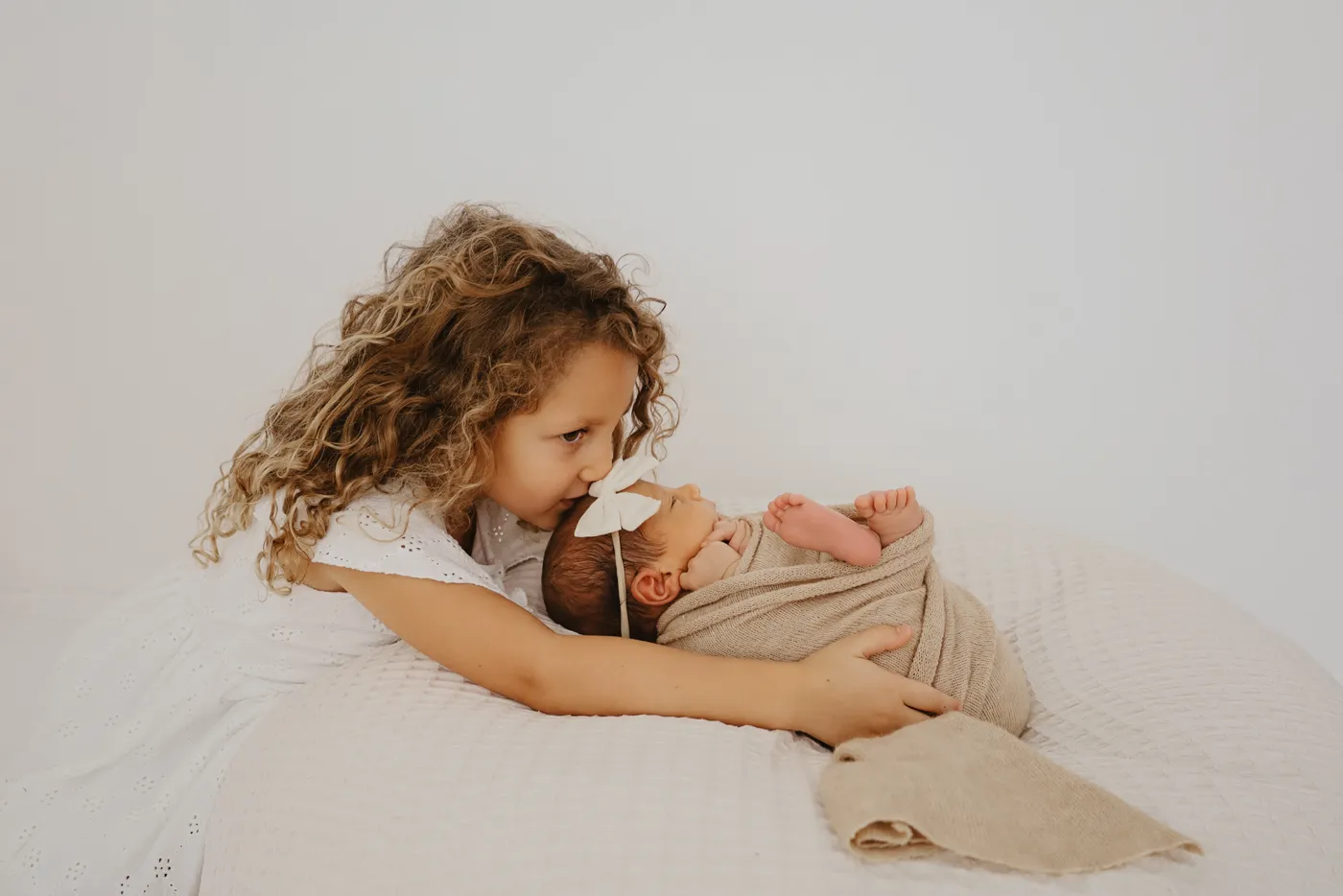 Große Schwester mit Locken kuschelt sich an ihr neugeborenes Geschwisterchen