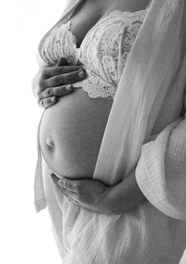 Schwarzweiß-Aufnahme eines Babybauchs, gehalten von beiden Händen, darüber Spitze